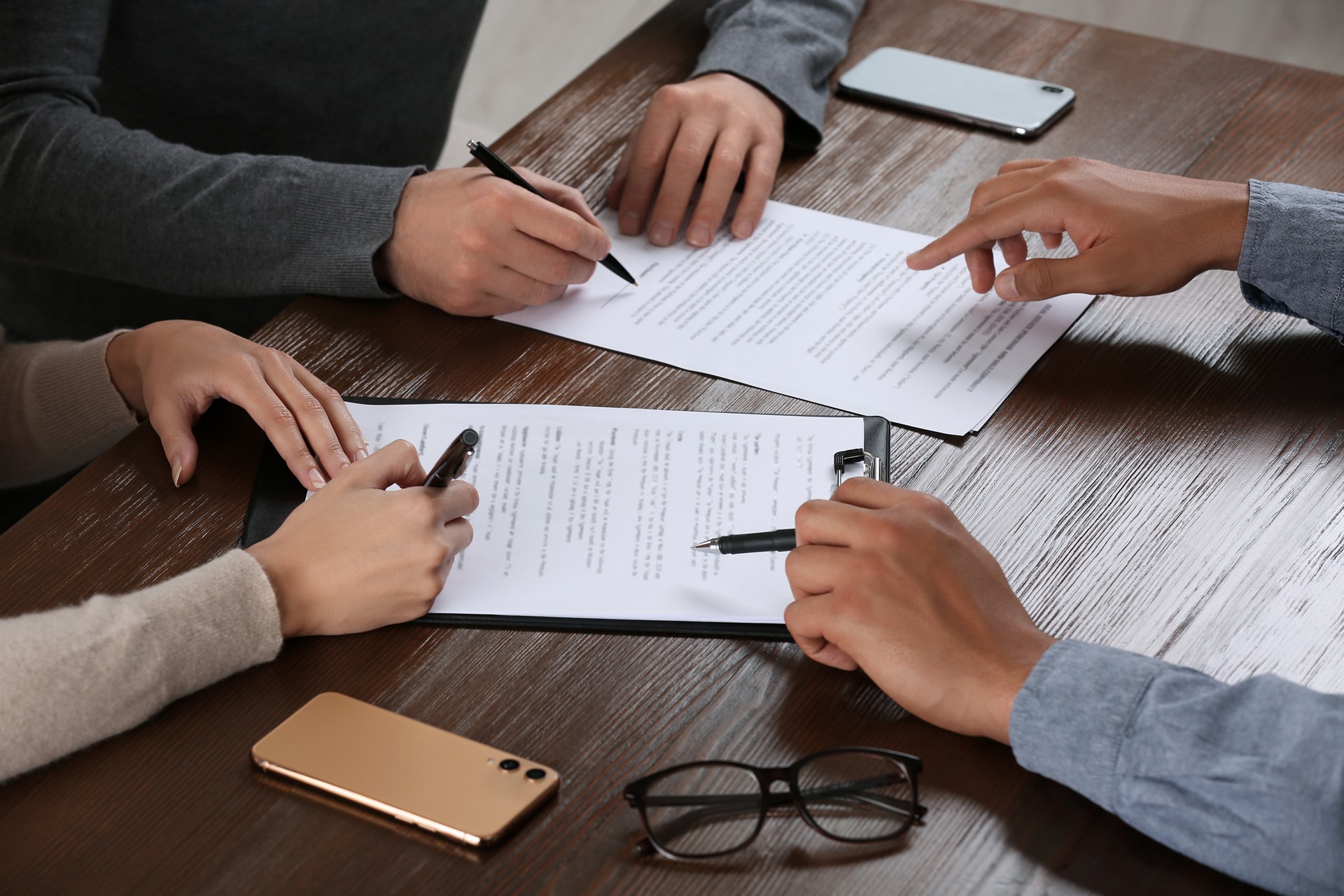 Notary helping couple with paperwork at wooden table, closeup